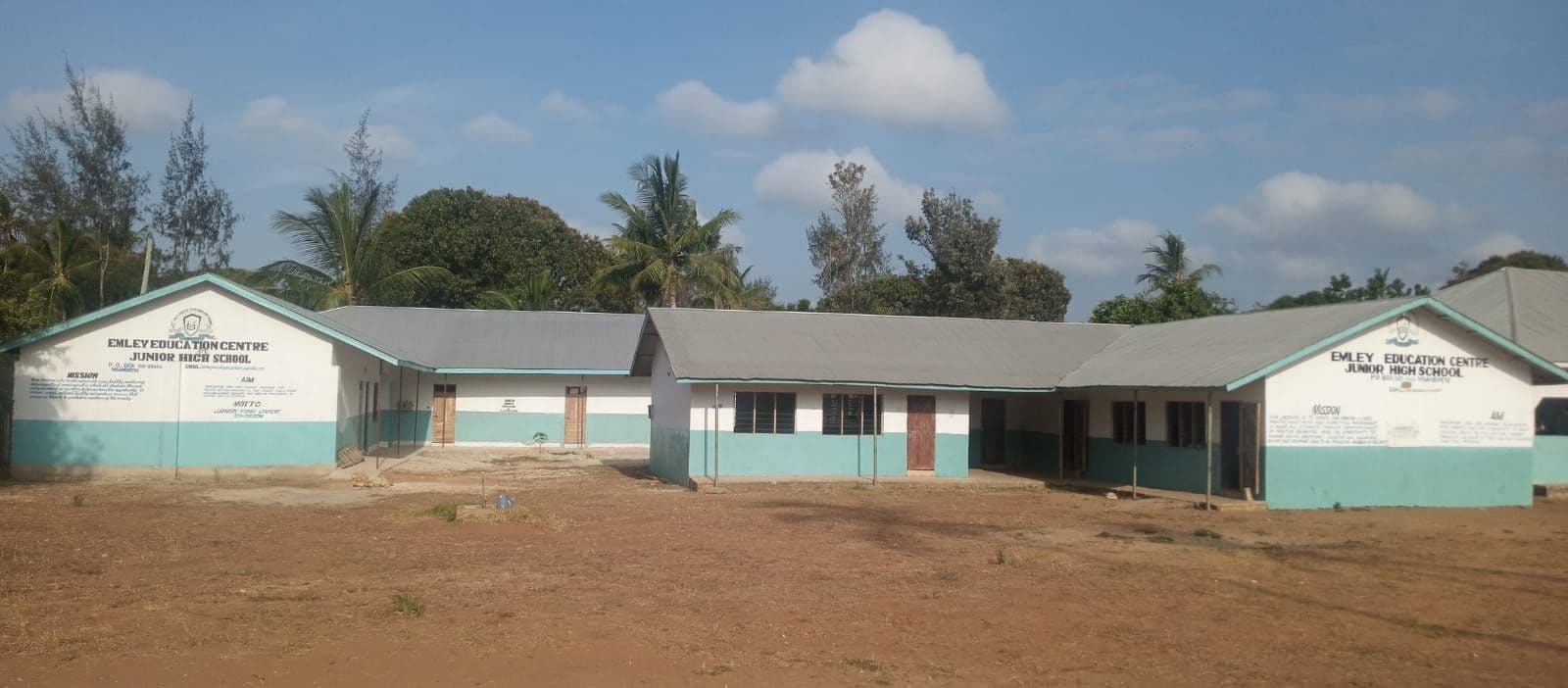 Long single-storey Emley Education Centre Junior High School buildings across a dusty yard under blue sky