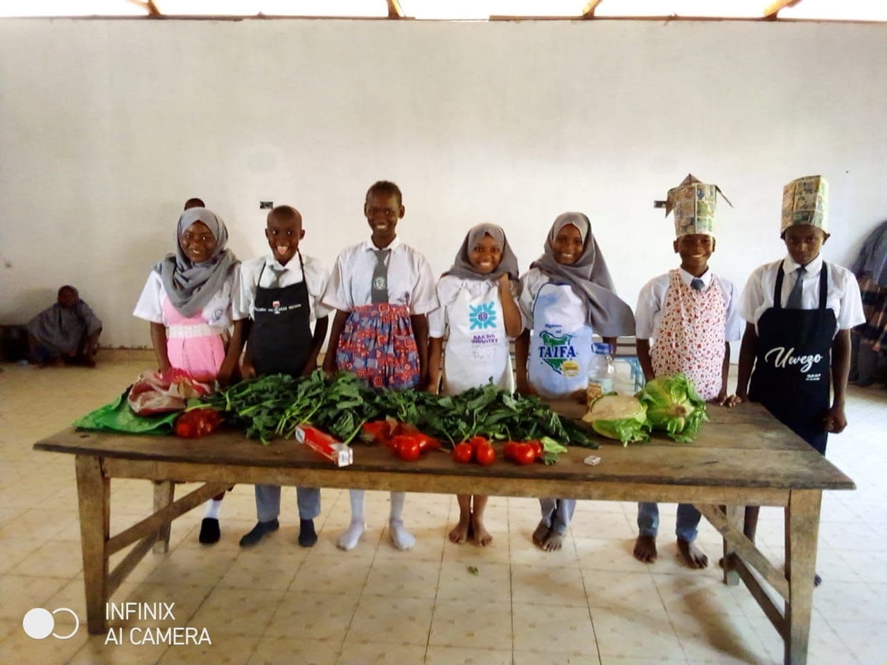 Pupils in aprons and paper chef hats behind a table of fresh vegetables