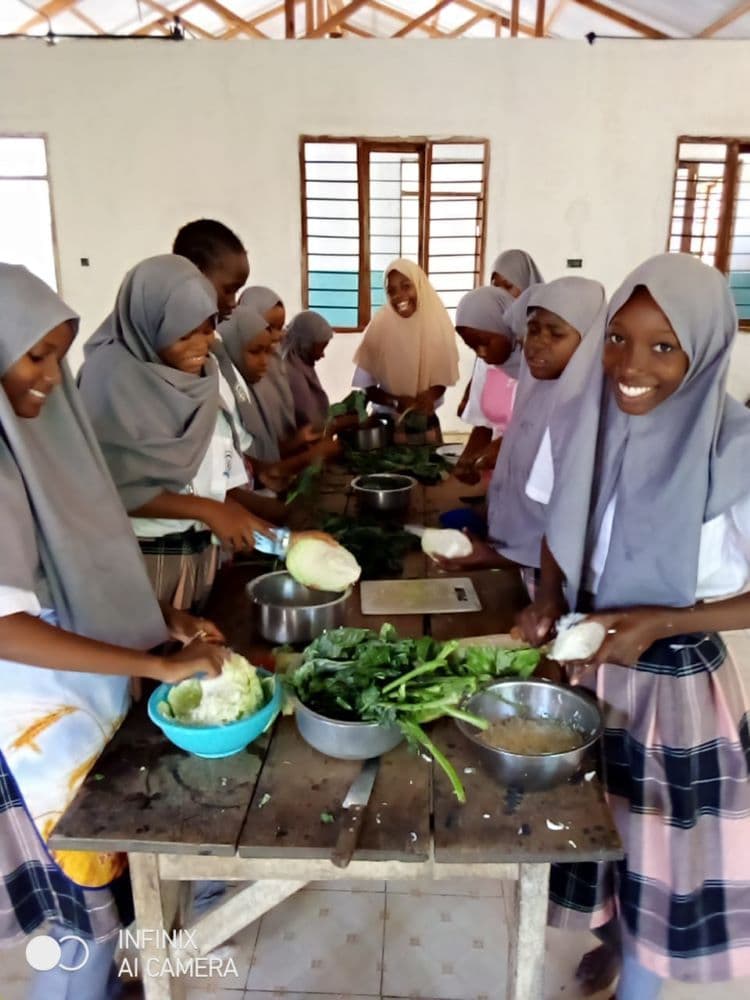 Girls in headscarves chopping cabbage and greens at a wooden table