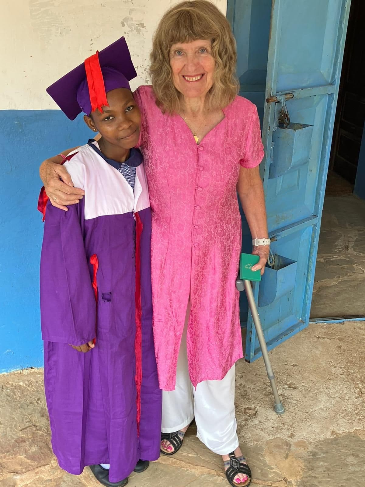 Dida in a purple graduation gown and cap standing arm in arm with a woman in pink