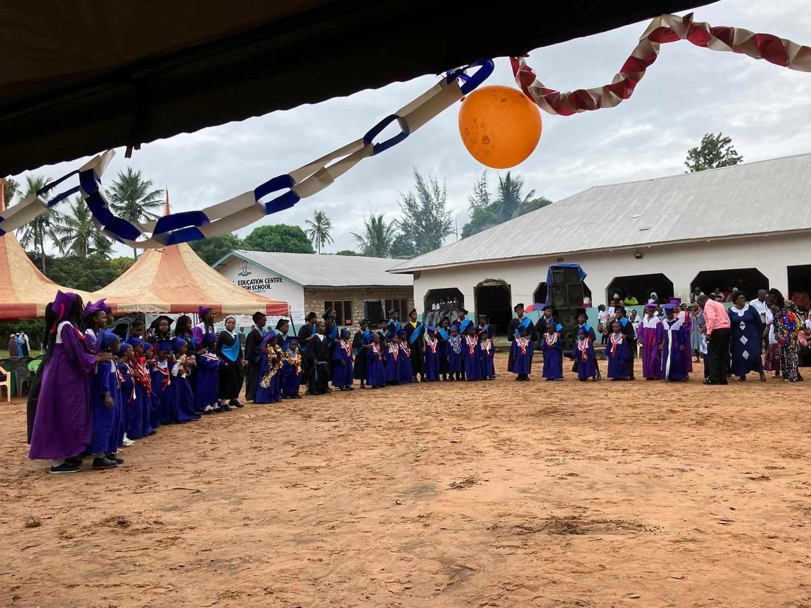 A long line of children in blue and purple graduation gowns in the school yard