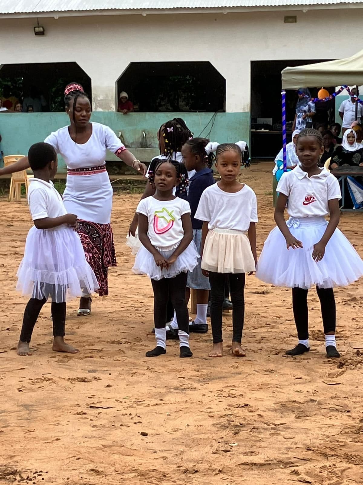 Young girls in white tutus dancing on sand with a woman behind them
