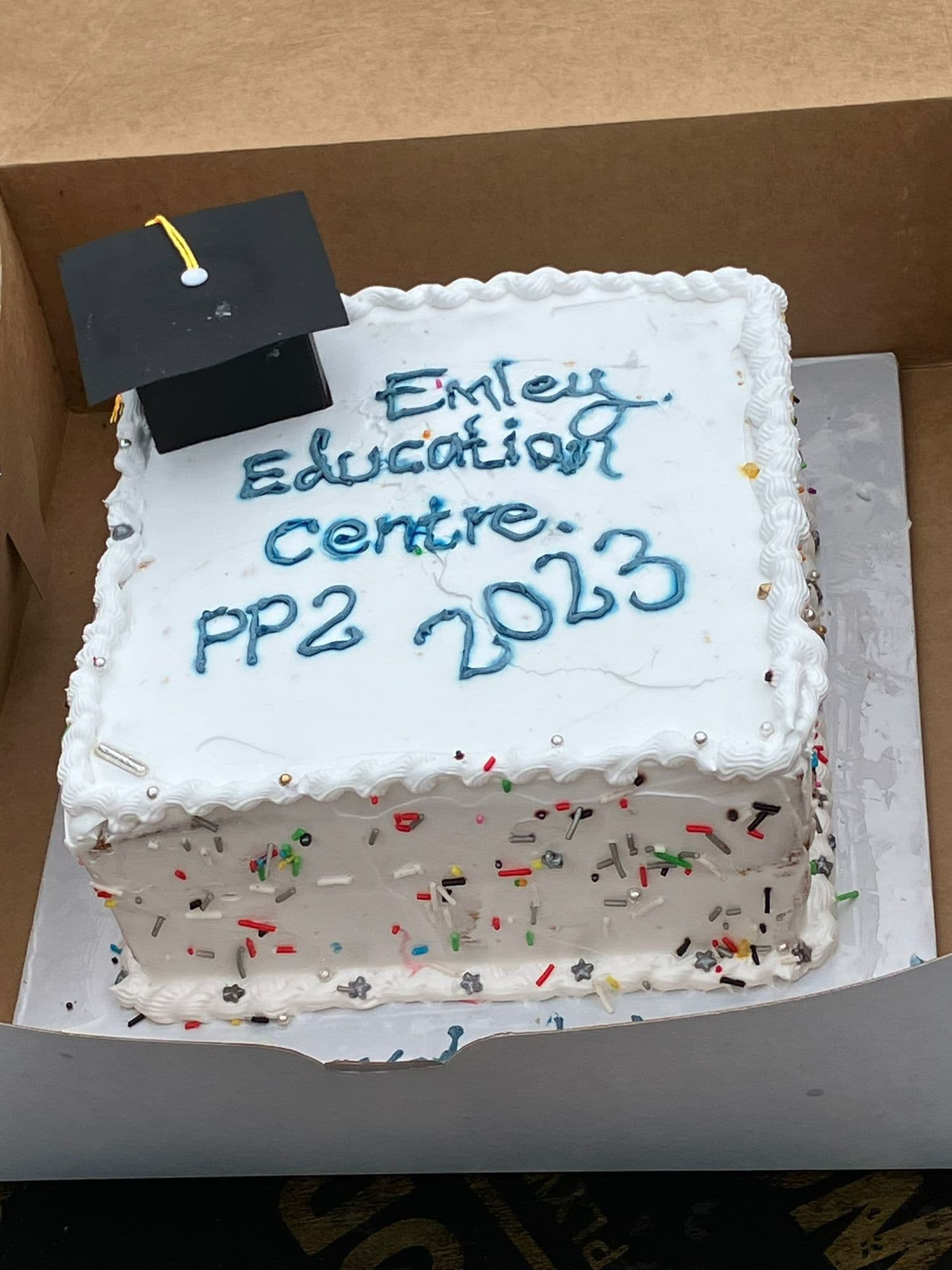 A boxed white cake iced 'Emley Education centre PP2 2023' with a small mortarboard on top