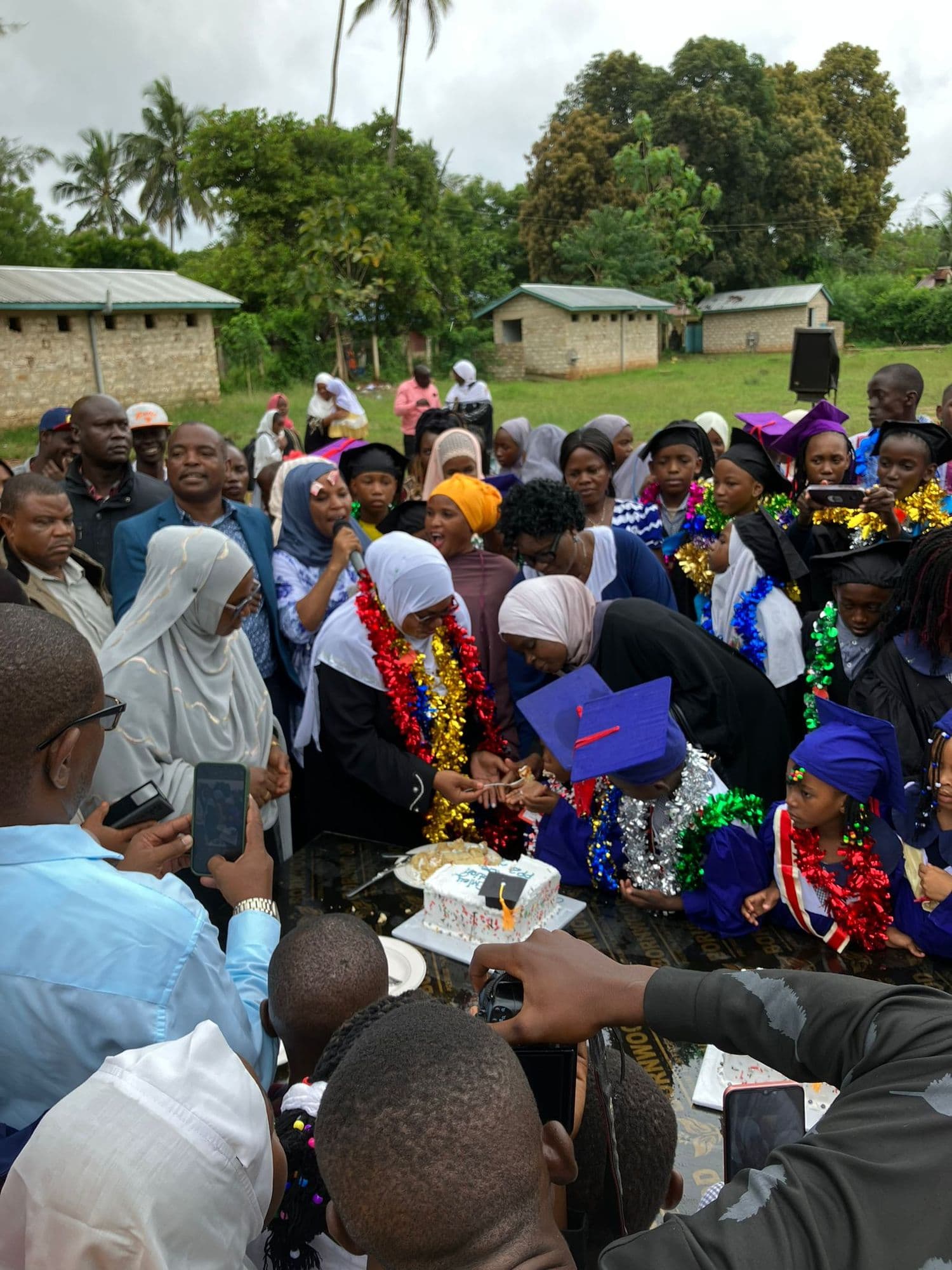 Crowd gathered as pupils in gowns and tinsel garlands are fed cake