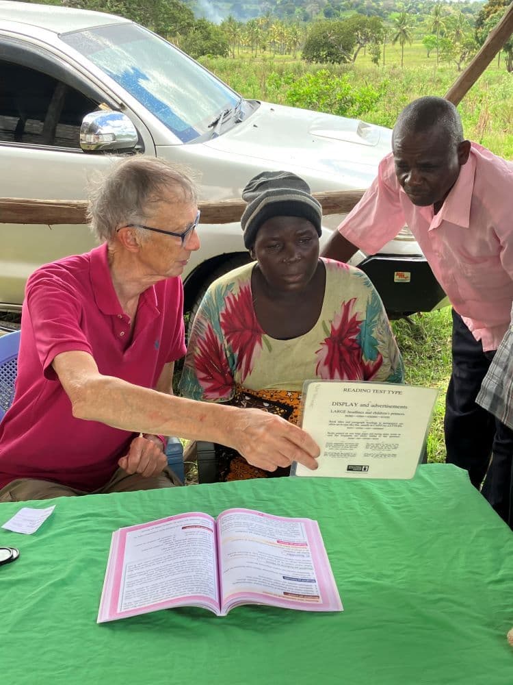 A volunteer shows a reading card to a woman at a green table outdoors