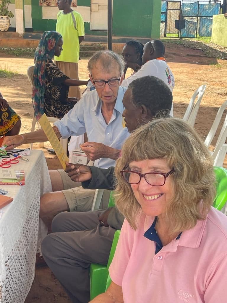 Two volunteers testing a man's eyes with reading cards at an outdoor camp