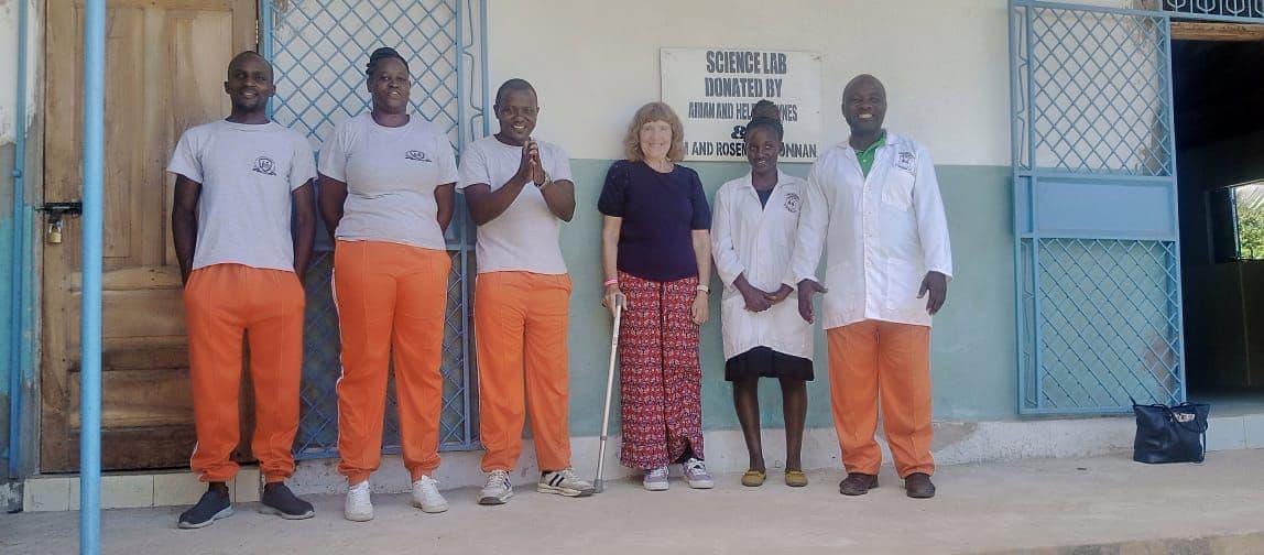Five teachers, two in lab coats, standing with a visitor outside the science lab door