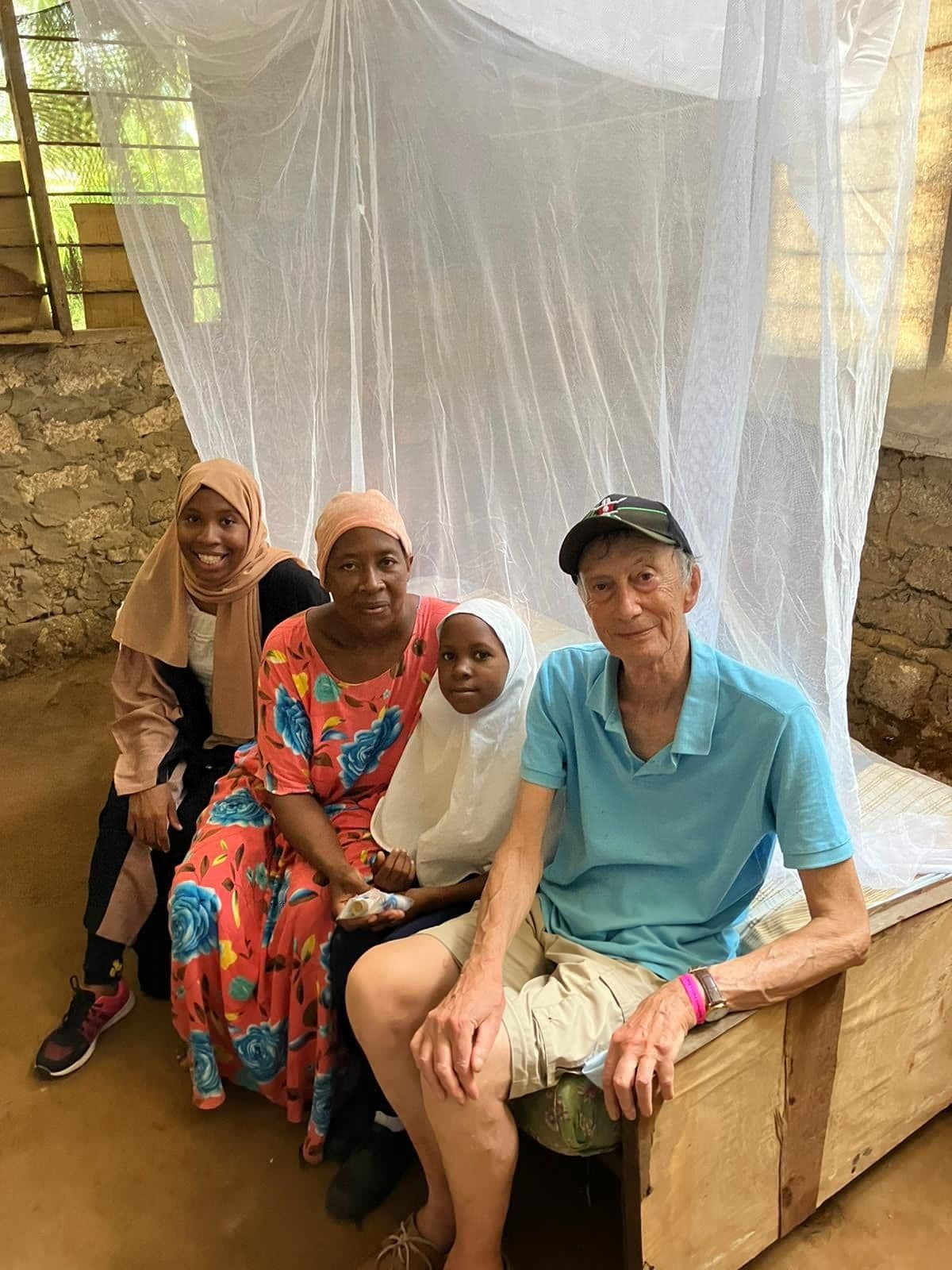 A man sitting with two women and a child on a bed under a new mosquito net