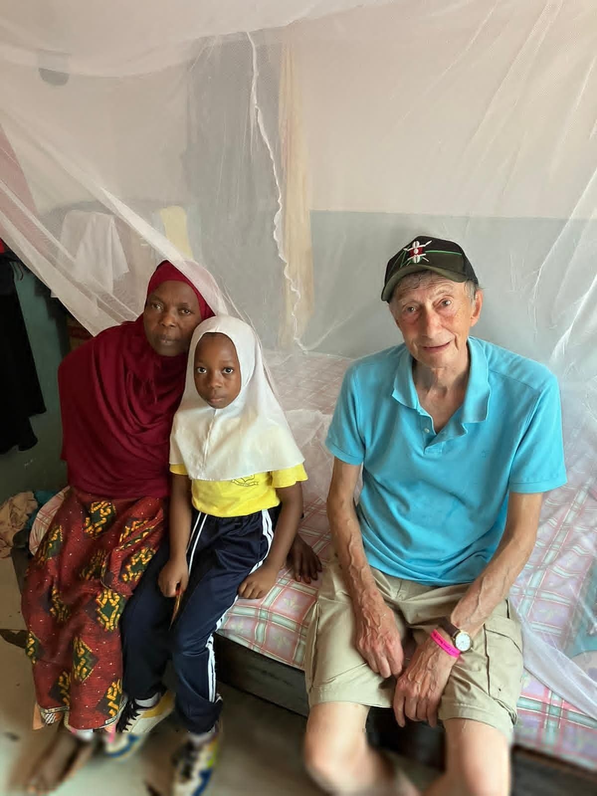 A man sitting with a woman and a girl on a bed under a white mosquito net