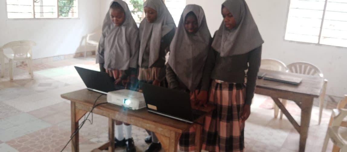 Four girls at a table using laptops connected to a projector