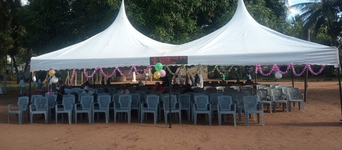 A large white marquee decorated with tinsel and balloons over rows of chairs on red earth