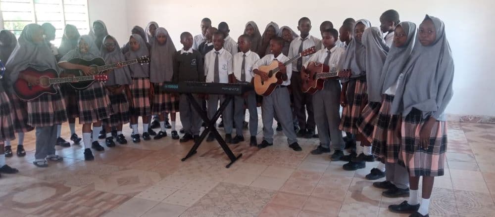 A large group of pupils gathered around guitars and a keyboard in a classroom