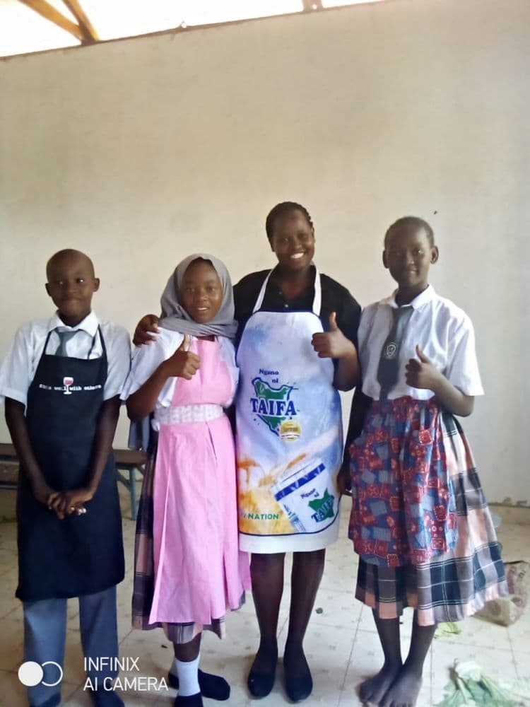 Three pupils in aprons giving a thumbs-up beside their teacher