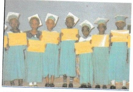 Seven nursery pupils in graduation caps and gowns holding their certificates