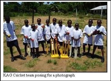 Pupils in white T-shirts holding cricket bats and balls, standing in a line on a grassy field
