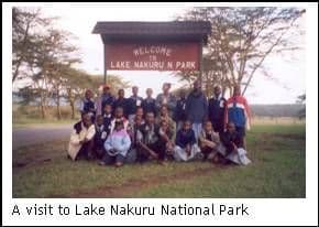 Pupils and teachers grouped on the grass in front of the Lake Nakuru National Park welcome sign