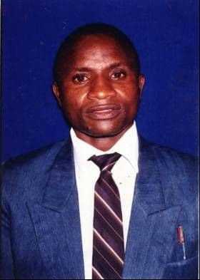 Portrait of Rev Francis Rai Ndoro in a grey suit and striped tie against a blue background