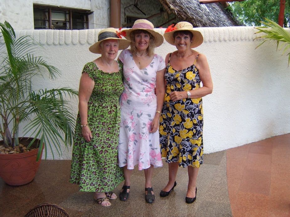 Three UK women in sun hats and summer dresses standing together on a veranda