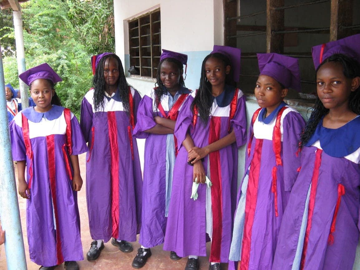Class 8 girls in purple graduation gowns and mortarboards standing in a row outside a classroom