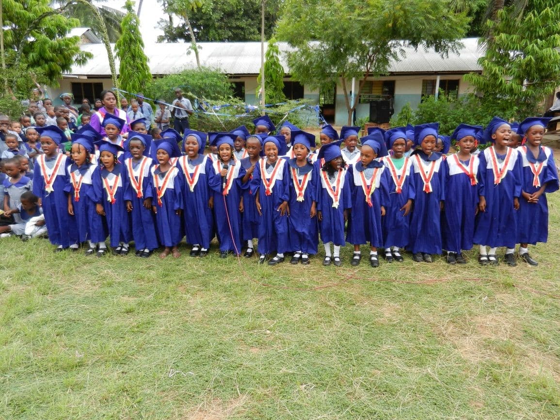 Nursery graduates in blue gowns and caps lined up on the school field