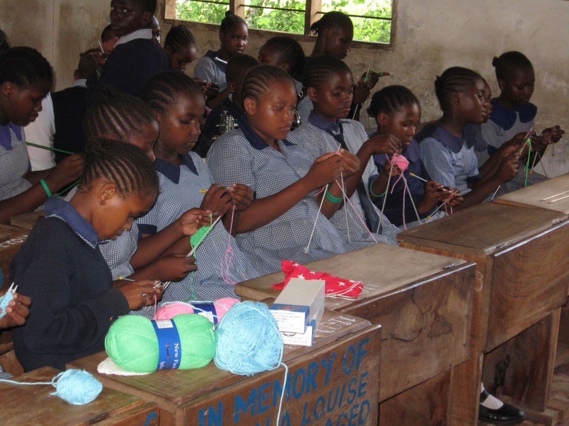 Girls in school uniform knitting with balls of wool at their classroom desks