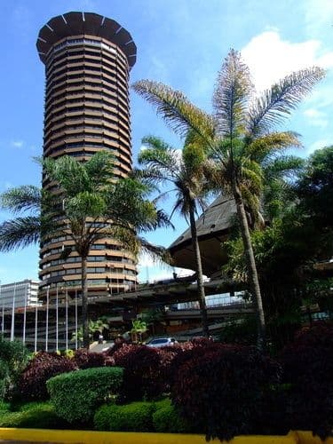 The cylindrical Kenyatta International Conference Centre tower in Nairobi behind palm trees