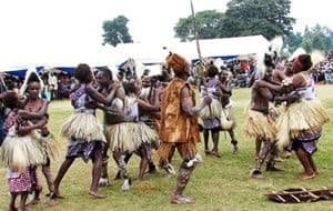 Dancers in grass skirts performing a traditional dance on a grassy field before a crowd