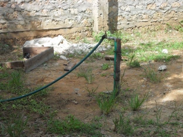 A water pipe and tap stand running along the base of a stone school wall