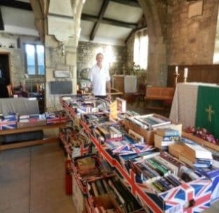 A man standing behind tables of second-hand books draped with Union flags