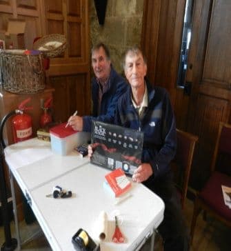 Two men seated at a table selling raffle tickets