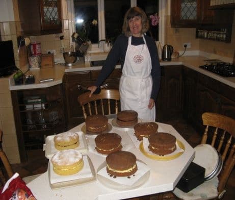 A woman in an apron in a kitchen with a table of sponge cakes