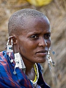 A Maasai woman with a shaved head wearing long beaded earrings and necklaces
