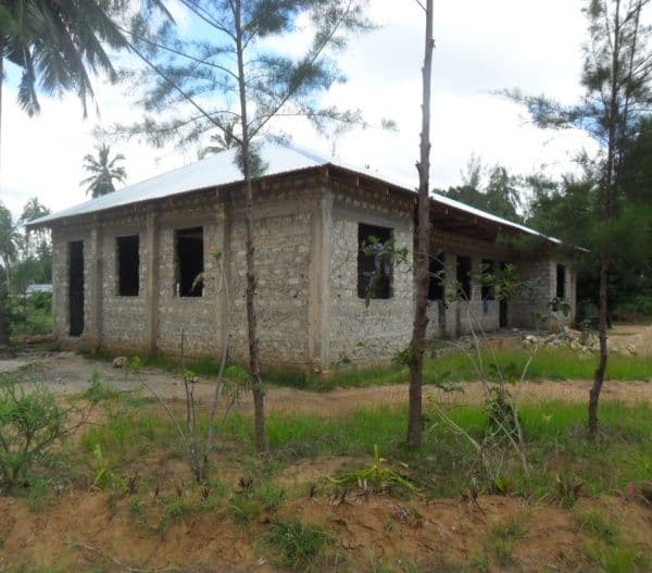 The roofed but unfinished stone library building among young trees
