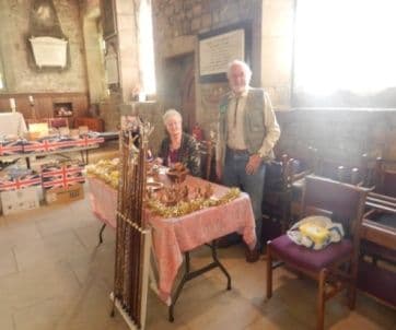 A man and a woman beside a table of African wood carvings in a church hall