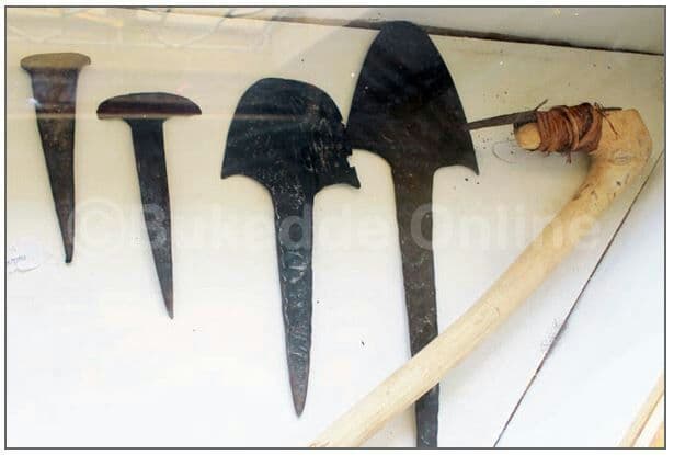 Traditional iron hoe and spear blades mounted on a wall beside an animal horn