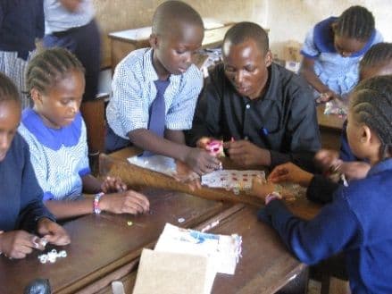 A teacher helping pupils make rubber band bracelets at a classroom desk