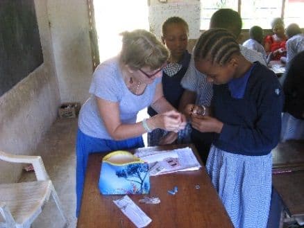 A visiting woman showing pupils how to make bracelets at a desk
