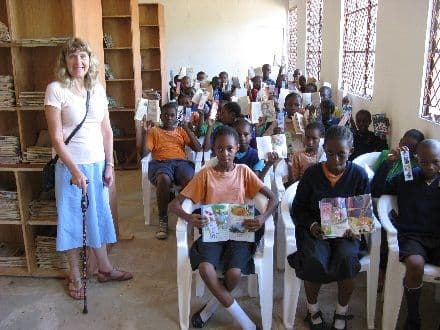Pupils seated in the library holding books and bookmarks while a visitor looks on