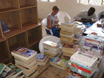 Stacks of books on a library table being catalogued beside empty shelves