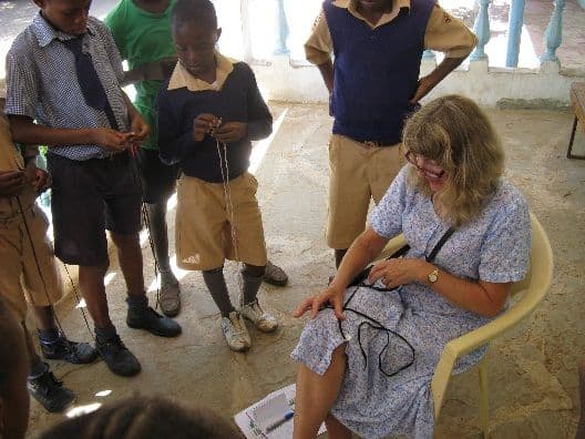 A visiting woman seated with scouts practising tying knots