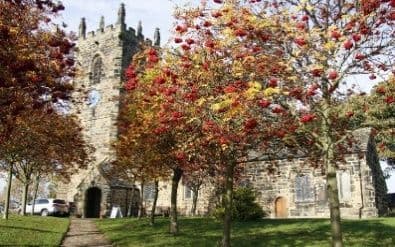 Stone church with a square tower behind trees in autumn colours