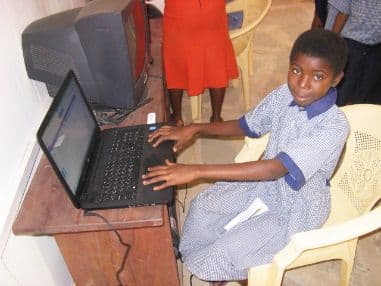 Pupil in a checked school uniform typing on a laptop at a desk