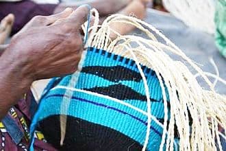 Close-up of hands weaving a blue and black patterned sisal basket