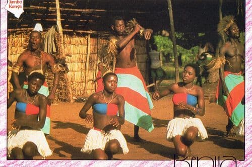 Dancers in grass skirts and red-and-blue costumes performing outside a thatched hut