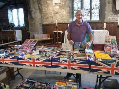 Man behind a stall of books draped with Union Jack bunting inside a church