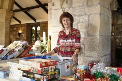 Woman standing behind a stall of board games, jigsaws and tinsel