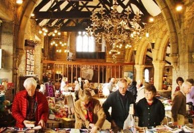 Shoppers browsing crowded sale stalls inside a timber-roofed church hall