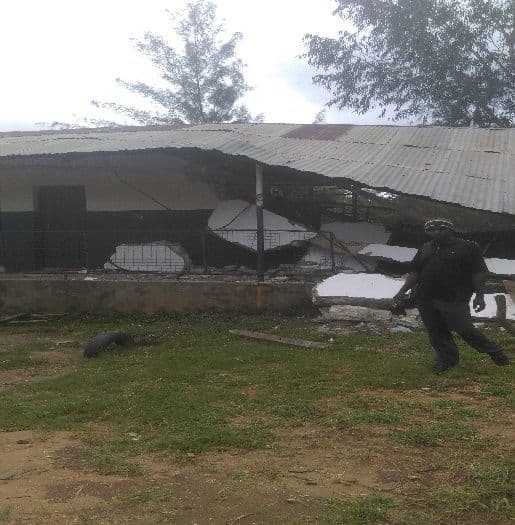 Partly demolished classroom with a collapsed roof and rubble beside a grassy yard