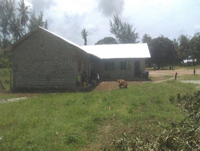 New stone classroom block with a white iron roof on a grassy school compound