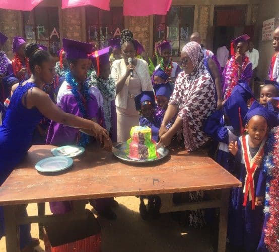 Graduating pupils in purple gowns and garlands gathered around a table with a decorated cake